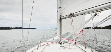 Fırtınada beyaz yat denize açılıyor. Direk görüntüsü, yelkenler, donanım. 9 metre İsviçre yapımı seyyar yelkenli. Yaz tatilleri, dinlenme, spor, boş zaman aktiviteleri.
