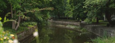 Kanal boyunca modern ahşap köprü (tahta köprü). Çiçek süsleme, kırmızı ve sarı çiçekler. Yeşil yaz parkı. Idyllic manzara. Turizm, dinlenme, çevre düzenlemesi, bahçe düzenlemesi.