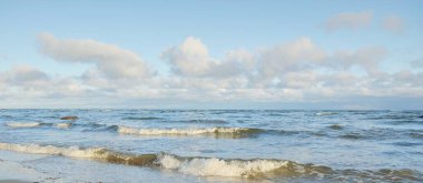Kışın Baltık Denizi 'nin panoramik manzarası. Parlayan kümülüs bulutlarıyla açık mavi gökyüzü. Su yüzeyi dokusu, dalgalar ve su yakından sıçrıyor. Kararsız hava, iklim değişikliği, doğa, deniz manzarası