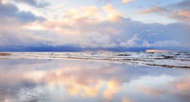 Kumlu bir sahilden Baltık Denizi 'nin panoramik manzarası. Açık günbatımı gökyüzü, parlak pembe bulutlar, yumuşak ışık. Suyun simetri yansımaları, doğal ayna. Hava, kış, iklim değişikliği, doğa
