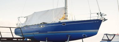 Açık bir kış gününde küçük bir limanda karada duran mavi şalopeli bir yat. Yeni yelken sezonunu bekliyorum. Sanayi, iş, ulaşım, hizmet, lojistik, spor, eğlence kavramları