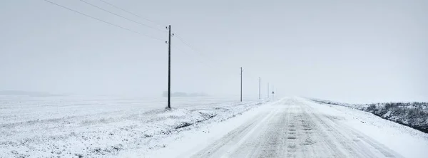 吹雪の後 フィールドを介して雪に覆われた田舎道 送電線 変圧器の棒 車からのパノラマビュー 暗い嵐の空 オフロード 冬のタイヤ リモート村 — ストック写真