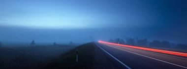 Gece sisli bir havada boş otobanın panoramik görüntüsü. Ay ışığı. Gün doğumu. Avrupa. Ulaşım, lojistik, seyahat, yolculuk, özgürlük, sürüş. Hareket bulanıklığı etkisi. Kırsal alan