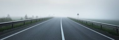 Gün doğumunda sisli bir havada boş otobanın tarlalar ve ormanlar arasındaki panoramik görüntüsü. Avrupa. Ulaşım, lojistik, seyahat, yolculuk, özgürlük, sürüş. Kırsal alan