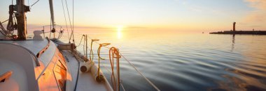 Günbatımında yağmurdan sonra beyaz yat denize açılacak. Güverteden pruvaya kadar yakın çekim. Durgun bir suya yansıyan parlak bulutlarla dolu berrak mavi bir gökyüzü. Idyllic deniz manzarası. Deniz, seyahat, seyahat yerleri