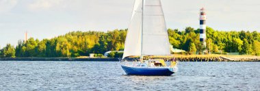 Gün batımında Riga körfezinde mavi yelkenli yelkenli yelkenli. Yakın plan. Baltık Denizi, Letonya. Arka planda deniz feneri var. Yarış, spor, eğlence, eğlence aktivitesi, takım çalışması kavramları.