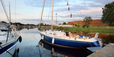 Zarif ve modern yelkenli tekneler (kiralık) açık bir günde yat limanındaki bir rıhtıma demirlediler. Ulaşım, spor ve eğlence teması. İsveç. Mavi yelkenli donanımlı yelkenli. Yakın plan.