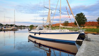 Günbatımında yat limanındaki bir rıhtıma demirlenmiş zarif ve modern yelkenli tekneler. Ulaşım, gezi, boş zaman aktivitesi, spor ve eğlence teması. İsveç
