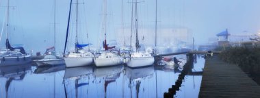 Yelkenli tekneler, güneşin doğuşunda yoğun beyaz bir sisle bir rıhtıma demirlediler. Kiel, Almanya 'daki yat kulübü. Spor, eğlence, ulaşım teması