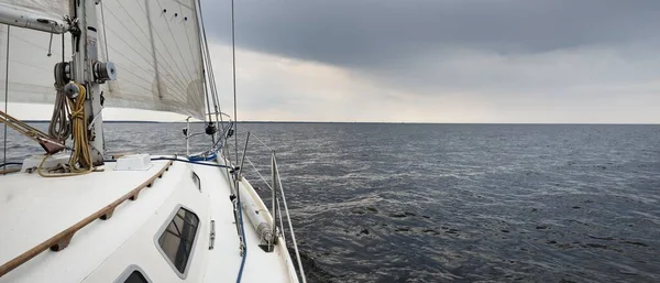 Beyaz yat dalgalı bir havada yelken açıyor güverteden pruva ve yelkenlere kadar yakın görüntü. Kuzey denizi, Norveç. Dramatik bulut manzarası. Yelkencilik, yarış, spor, eğlence, eğlence etkinliği teması