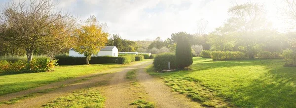 Kamp alanına giden tek şeritli kırsal bir yol, arka planda yeşil ve altın ağaçlar. Açık mavi gökyüzü. Normandiya, Fransa. Sonbahar tatilleri, boş zaman aktiviteleri, dinlenme, karavan, yolculuk, eko-turizm.