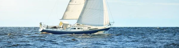 Blue sloop rigged yacht sailing in an open Baltic sea on a clear day, close-up. Riga bay, Latvia. Cruise, sport, recreation, leisure activity concepts