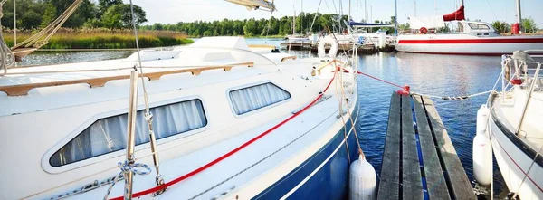 Zarif ve modern yelkenli tekneler (kiralık) açık bir günde yat limanındaki bir rıhtıma demirlediler. Ulaşım, spor ve eğlence teması. İsveç. Mavi yelkenli donanımlı yelkenli. Yakın plan.