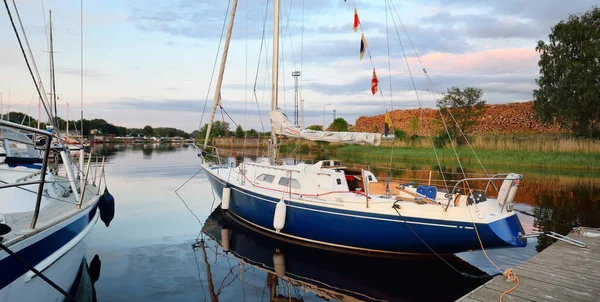 Zarif ve modern yelkenli tekneler (kiralık) açık bir günde yat limanındaki bir rıhtıma demirlediler. Ulaşım, spor ve eğlence teması. İsveç. Mavi yelkenli donanımlı yelkenli. Yakın plan.