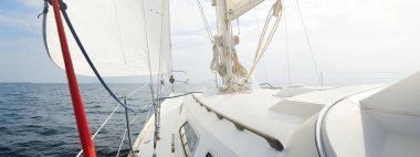 Güneşli bir yaz gününde beyaz bir yat denize açılıyor. Güverteden pruvaya, direğe ve yelkenlere yakın görüntü. Dalgalar ve su sıçramaları. Açık mavi gökyüzü. Finlandiya Körfezi