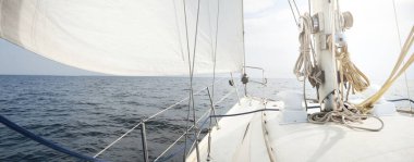 Güneşli bir yaz gününde beyaz bir yat denize açılıyor. Güverteden pruvaya, direğe ve yelkenlere yakın görüntü. Dalgalar ve su sıçramaları. Açık mavi gökyüzü. Finlandiya Körfezi