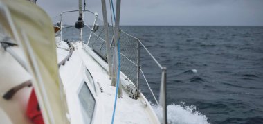 Fırtına sırasında yat gezintisi. Güverteden pruvaya yakın görüntü, direk, yelkenler. Dramatik gökyüzü, kara bulutlar, dalgalar, su sıçramaları. Kuzey denizi, Norveç. Destansı deniz manzarası. Kötü hava