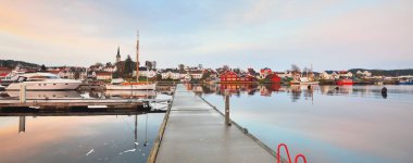 Yelkenli ve balıkçı tekneleri gün batımında yat limanındaki bir rıhtıma demirlediler. Renkli bulutlar, suda yansımalar. Yelkencilik, eğlence teması. Güney Norveç Köyü