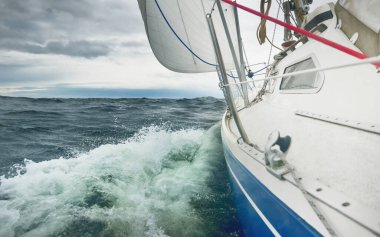 Yağmurlu bir günde, fırtınalı bir havada yat gezintisi. Güverteden pruvaya, direğe ve yelkenlere yakın görüntü. Dramatik fırtınalı gökyüzü, kara bulutlar. Dalgalar ve su sıçramaları. Kötü hava. Baltık Denizi, İsveç