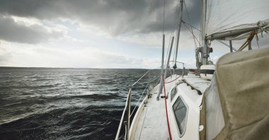 Fırtına sırasında yat gezintisi. Güverteden pruvaya yakın görüntü, direk, yelkenler. Dramatik gökyüzü, kara bulutlar, dalgalar, su sıçramaları. Kuzey denizi, Norveç. Destansı deniz manzarası. Kötü hava