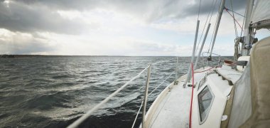 Fırtına sırasında yat gezintisi. Güverteden pruvaya yakın görüntü, direk, yelkenler. Dramatik gökyüzü, kara bulutlar, dalgalar, su sıçramaları. Kuzey denizi, Norveç. Destansı deniz manzarası. Kötü hava