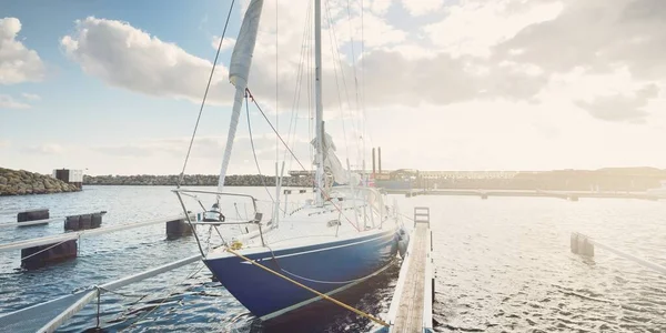 Blue sloop rigged sailboat (for rent) moored to a pier in a yacht marina on a clear day, close-up. Transportation, sport and recreation theme. Ystad, Sweden