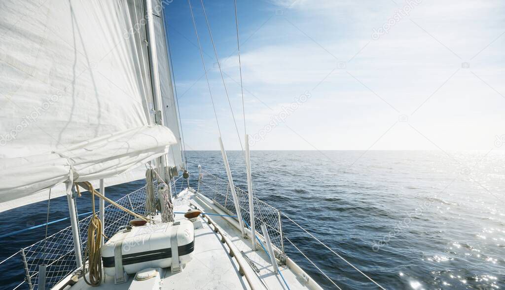 White yacht sailing on a sunny day. Top down view from the deck to the bow and sails. Waves and water splashes. Clear blue sky. North sea, Norway. Transportation, sport, recreation theme