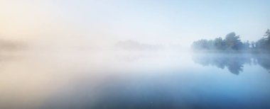 Kalın beyaz bir sis içinde orman gölünün resim gibi manzarası. Sudaki yansımalar. Saf altın güneş ışığı. Atmosferik manzara. Sonbahar sezonu. Avrupa 'da doğa, ekoloji ve çevre koruma