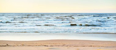 Gün batımında Baltık kıyısı manzarası. Kum tepeleri ve bitkiler yakın plan. Açık mavi akşam gökyüzü. Dalgalar ve su sıçramaları. Idyllic deniz manzarası. Letonya