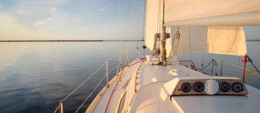Günbatımında yağmurdan sonra beyaz yat denize açılacak. Güverteden pruvaya kadar yakın çekim. Durgun bir suya yansıyan parlak bulutlarla dolu berrak mavi bir gökyüzü. Idyllic deniz manzarası. Deniz, seyahat, seyahat yerleri