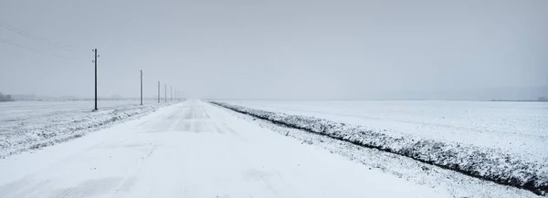 暴风雪过后 覆盖着白雪的乡间小路穿过田野 变压器杆 从车上俯瞰全景 黑暗的暴风雨的天空 冬季轮胎 偏远村庄 — 图库照片