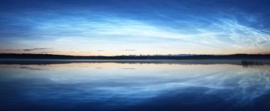 Yaz gündönümü gecesinde Saimaa Gölü 'nün üzerinde gece parlayan bulutlar ve sis vardı. Ağaç siluetleri. Altın güneş ışığı. Uzun pozlama. Destansı bulut manzarası. Suyun simetri yansımaları. Finlandiya