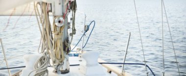 Açık bir günde açık denizde yelken açan beyaz yelkenli bir yat. Güverteden pruvaya bir manzara, direk, yelkenler. Ulaşım, seyahat, gezi, spor, eğlence, boş zaman aktivitesi, yarış, yelkenli yarışı