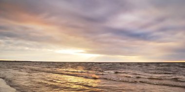 Dramatik günbatımı bulutları altında fırtınalı Baltık Denizi. Kumlu sahilden bir manzara. Riga Körfezi, Letonya. Destansı deniz manzarası. Karanlık sonbahar sahnesi. Meteoroloji, ekoloji, çevre koruma, iklim değişikliği