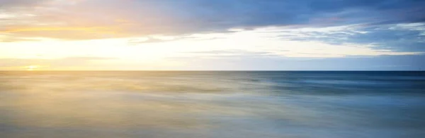 日没のバルト海 劇的な夕暮れの空 青と金色の雲 柔らかい日差し 水しぶき 絵のような夢のような風景 雲の風景 パノラマビュー 長時間露光 — ストック写真
