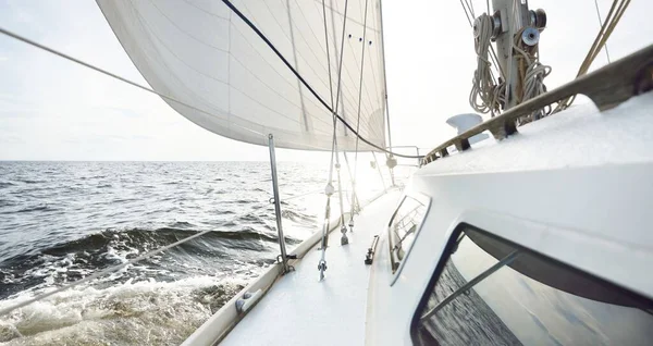 夏日阳光明媚 白色游艇在开阔的海面上航行 从甲板到船头和船帆的近景 浪花和水花四溅 晴朗的蓝天 有卷云和飞机轨道 — 图库照片