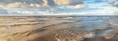 Gün batımında fırtınadan sonra Baltık kıyıları üzerinde parlayan kümülüs bulutlarıyla açık bir gökyüzü. Dramatik bulut manzarası. Sıcak altın güneş ışığı. Resimli bir manzara var. Hava kararsız. Uzun pozlama