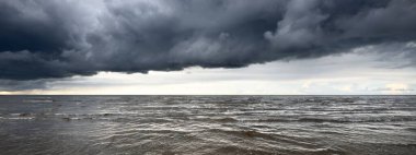 Gün batımında fırtınadan sonra Baltık Denizi kıyısında bir sürü koyu renkli kümülüs bulutu olan açık bir gökyüzü. Dramatik bulut manzarası. Resimli bir manzara var. Kararsız hava, mevsimler, iklim değişikliği