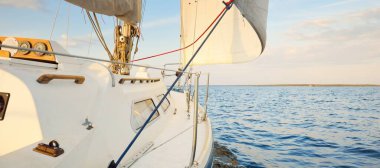 Gün batımında denize açılacak mavi şalopalı yat. Gökyüzü açık. Güverteden pruvaya bir manzara, direk, yelkenler. Ulaşım, seyahat, gezi, spor, eğlence, boş zaman aktivitesi, yarış, yelkenli yarışı