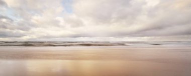 Baltık Denizi 'nin üzerinde parlak, altın renkli günbatımı bulutları. Dramatik bir gökyüzü. Kum, dalga ve su yüzeyi dokusu. Idyllic deniz manzarası. Kavramsal görüntü, uzun pozlama. Resimli panoramik manzara