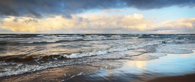 Gün batımında karla kaplı Baltık deniz kıyısından bir manzara. Riga Körfezi, Letonya. Renkli dramatik bulut manzarası. Derin hortum, sert hava, dalgalar ve su sıçramaları. Kış turizmi, küresel ısınma teması