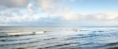 Kışın Baltık Denizi 'nin panoramik manzarası. Parlayan kümülüs bulutlarıyla açık mavi gökyüzü. Su yüzeyi dokusu, dalgalar ve su yakından sıçrıyor. Kararsız hava, iklim değişikliği, doğa, deniz manzarası