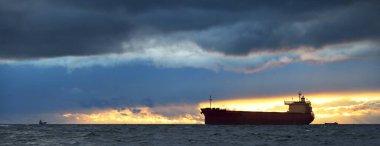 Büyük kırmızı kargo gemisi karanlık günbatımı göğünün altında açık denizde yol alıyor. Southampton 'da. İngiltere. Dramatik bulutlar, kasırga, fırtınalı hava. Küresel iletişim, nakliye, endüstri, lojistik