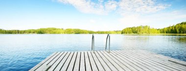 Nehrin yakınındaki ahşap iskele. Arka planda Evergreen kozalaklı orman var. Açık mavi gökyüzü, suda yansımalar. Idyllic yaz manzarası. Eko turizm, eğlence teması. Finlandiya