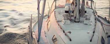 Gün batımında sakin bir suda yüzen mavi bir yat. Yakın plan. Gece yarısı güneşi. Sıcak akşam renkleri, suda yansımalar. Boş zaman aktivitesi, yaz tatili teması. Baltık Denizi, İsveç