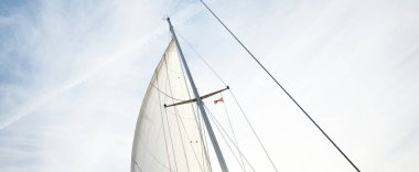 Beyaz yat yelkenlerinin alçak açılı görüntüsü. Sirus bulutları ve uçak izleri olan açık mavi bir gökyüzü. Hollanda