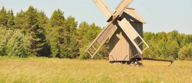 Açık bir yaz gününde, açık mavi gökyüzüne karşı tarlada eski bir ahşap yel değirmeni. Saaremaa, Estonya. Kavram sanatı, geleneksel zanaat ve alternatif üretim, çevre koruma, tarih