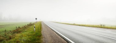 Gün doğumunda sisli bir havada boş otobanın arabasından ormana ve tarlalara doğru panoramik bir manzara. Avrupa. Ulaşım, lojistik, seyahat, yolculuk, özgürlük, sürüş. Kırsal alan