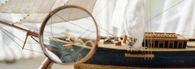 Retro bakır renkli büyüteç (el lensi) ve ahşap uzun gemi ölçekli yakın çekim. Klasik natürmort. Yelken, seyahat, yön bulma. Koleksiyon, hatıra, optik