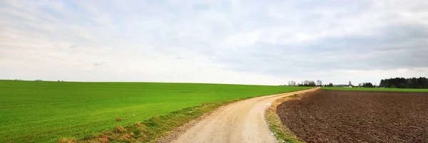 緑豊かな田園農業を通る未舗装の道路は日没時に畑を耕した 劇的な雲景 田舎の風景 暖かい冬だ 気候変動のテーマ ラトビア — ストック写真